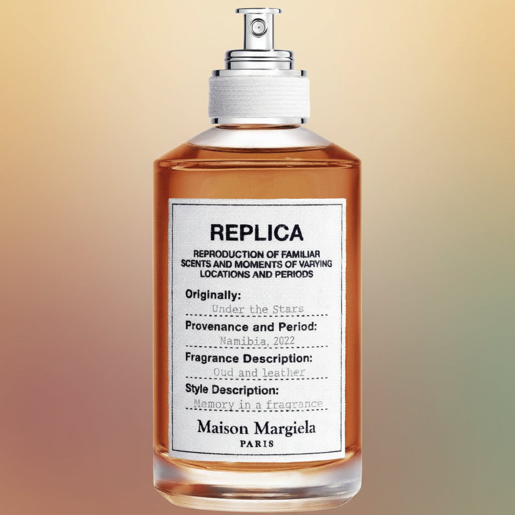 Maison Margiela Under the Stars perfume bottle full of amber liquid with a silver sprayer top on a warm gradient background.