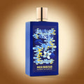 Blue perfume bottle with a two-tone blue and yellow design on the face, a gold cap and the words "Tobacco Flirting with Vanilla Talk Smoky to me" on a warm gradient background